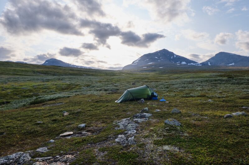 Lightweight backpacking tent pitched in a grass field surrounded by mountains