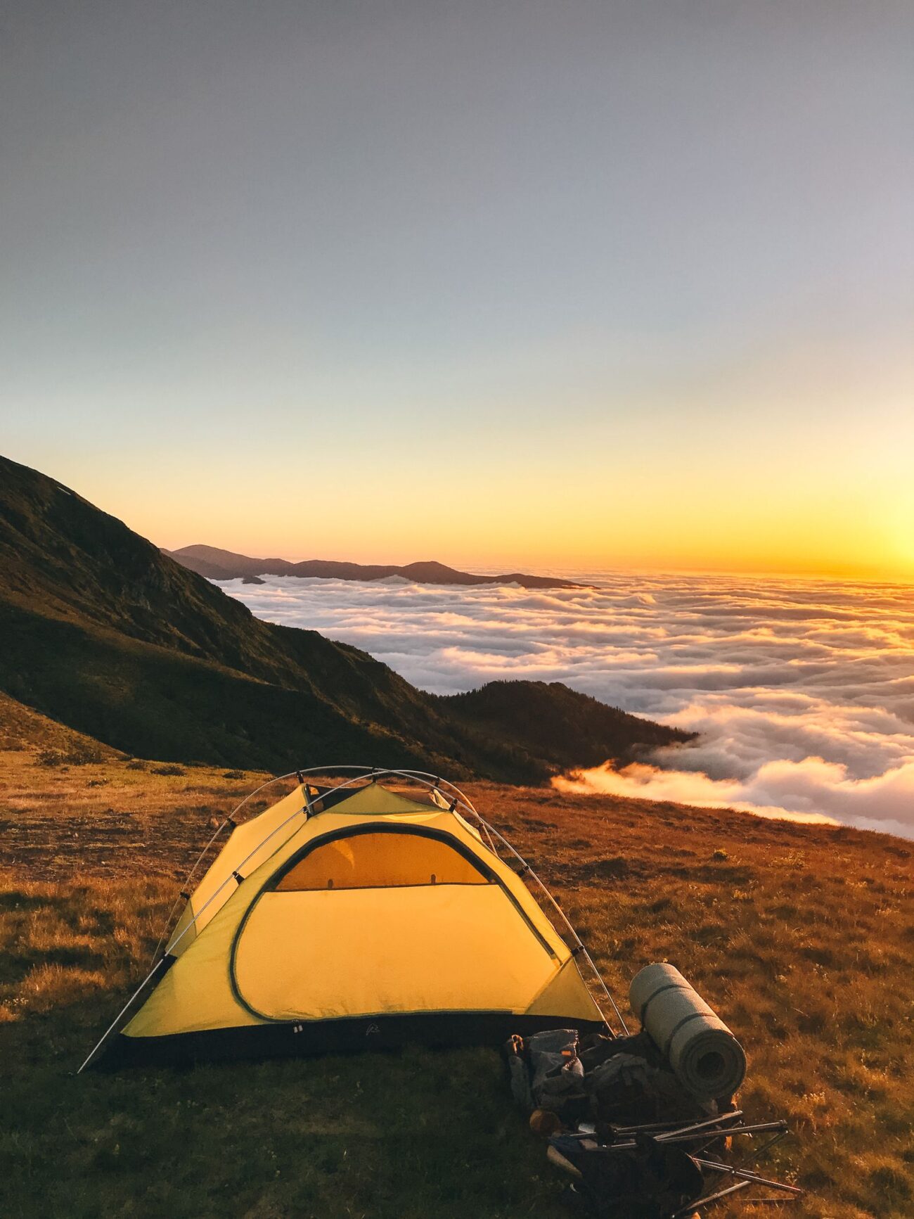 Yellow backpacking tent pitched on a mountain ridge at sunset above the clouds