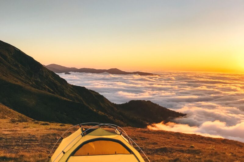 Yellow backpacking tent pitched on a mountain ridge at sunset above the clouds