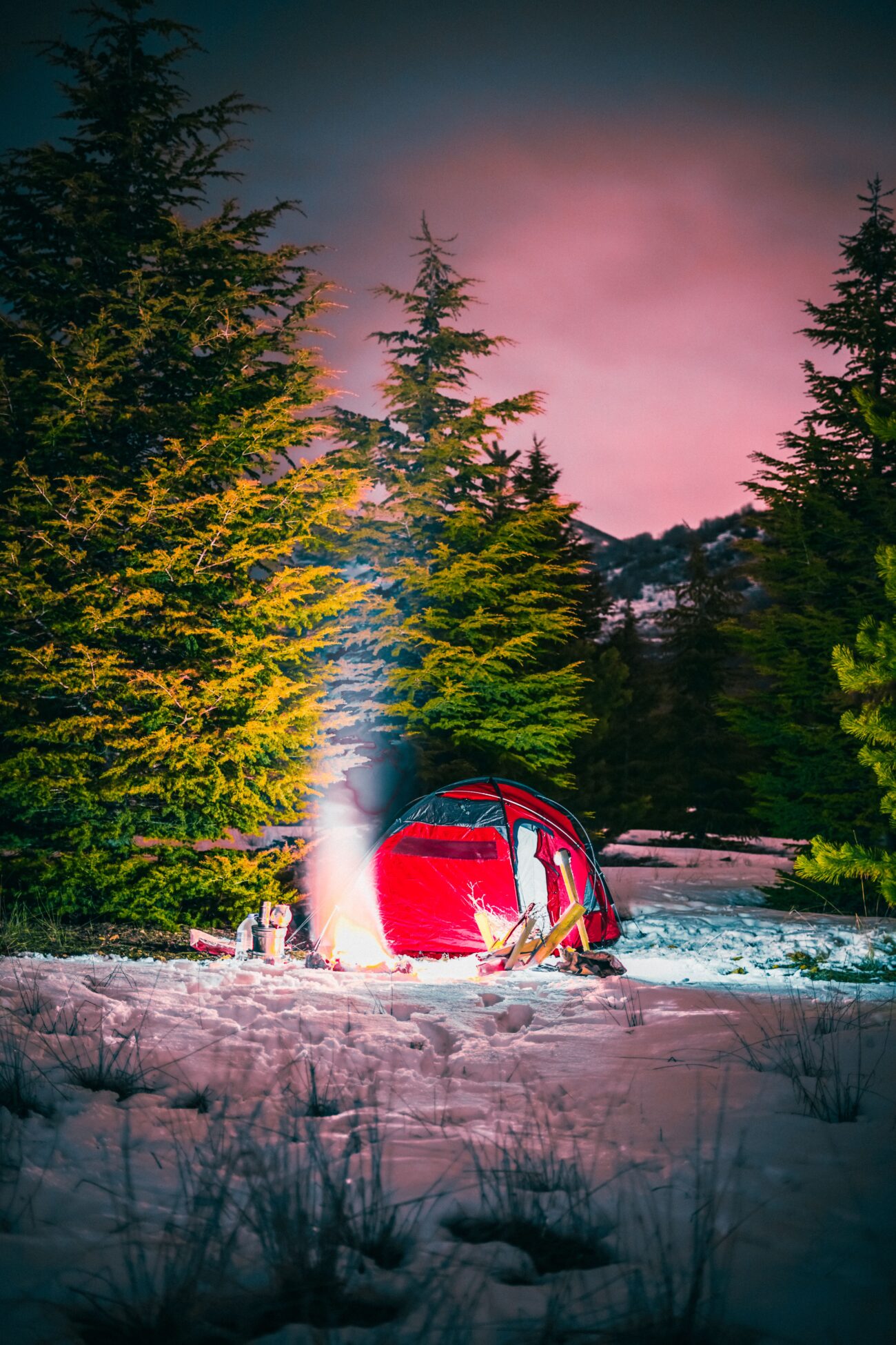 Red tent pitched among snow-covered trees at night during winter camping